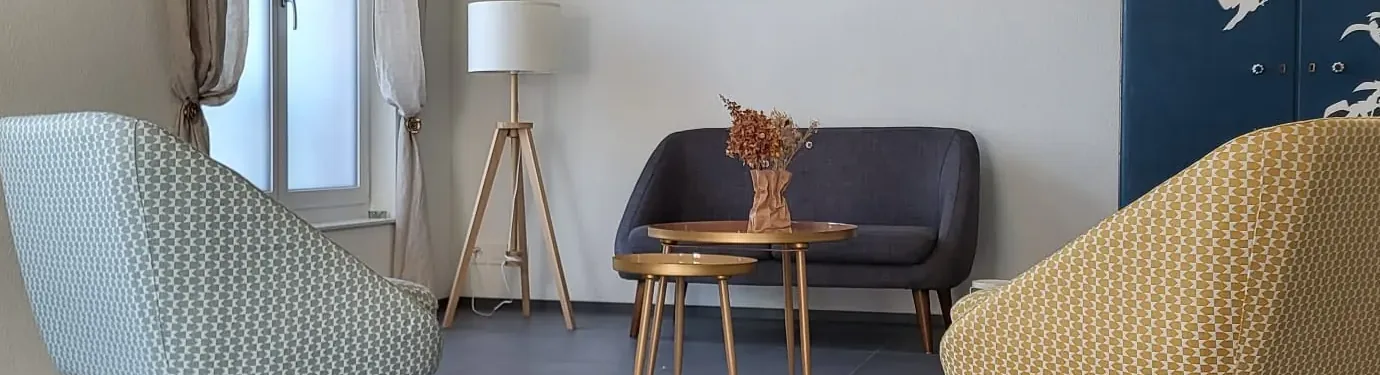 Therapieraum der Praxis mit Sofa, Sesseln, Stehlampe und kleinen Tischen